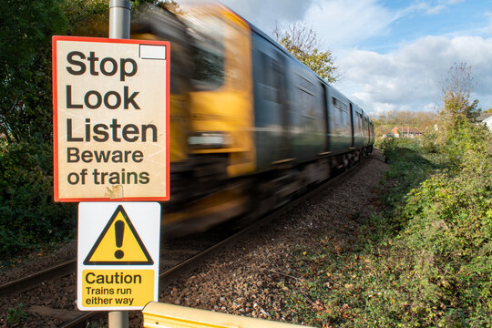 Train level crossing safety sign. Stop Look Listen warning sign crossing train tracks. selective focus on warning sign with a train passing with motion blur. Rail safety beware of trains signage.