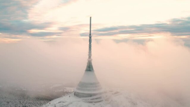 Futuristic Jested tower built on top of forestry mountain near Liberec. Dense fog surrounds modern construction with spire in winter aerial view