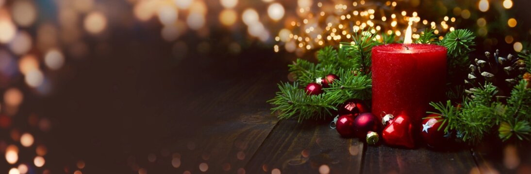 Christmas background - Red burning Advent Candle with fir branches on wooden board  -  Magic bokeh light frame - header, banner, panorama with copy space - first Advent