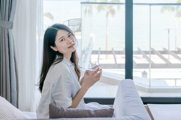 Asian woman holding a glass of water and sitting on sofa