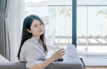 Asian woman holding a glass of water and sitting on sofa