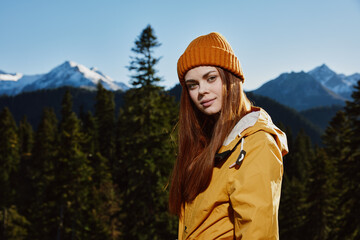 Young woman tourist portrait in yellow raincoat traveling and hiking in the mountains. Hiking in nature in the sunset