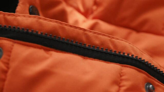 Close-up details of orange waterproof fabric of winter jacket, down jacket. Zipper on the jacket, rivet button. Textile, material, clothing production. Fashion, Style. Clothes background