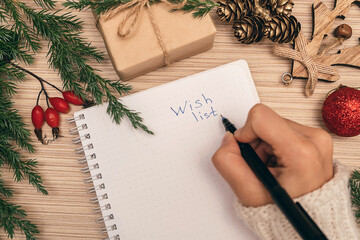A woman writing a wish list in a notebook, hands close-up, top view.Holiday decorations.New Year...