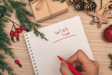 A woman writing a wish list in a notebook, hands close-up, top view.Holiday decorations.New Year and Christmas concept.Planning concept.