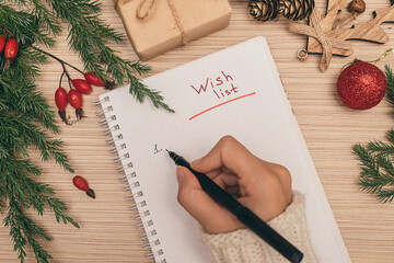 A woman writing a wish list in a notebook, hands close-up, top view.Holiday decorations.New Year and Christmas concept.Planning concept.