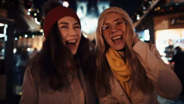 Two cheerful multiracial girls hug, hold sparklers and laugh in the middle of a Christmas-dressed-up party to the chiming of the chimes on New Year's Eve. Concept LGBT happiness freedom love