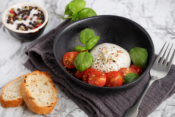 Fresh Italian burrata with tomatoes and basil on plate on marble table, close up. Burrata cheese ball made from mozzarella and cream. Healthy food