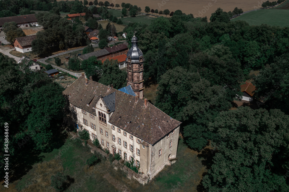 Poster an aerial view of a large building with a tower and a clock on it's side and trees surrounding it.