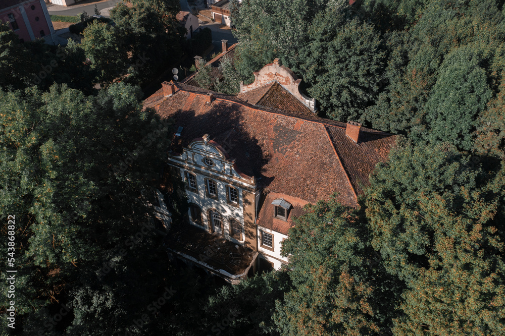 Poster a large building surrounded by trees in a forest area with a brown roof and a tall tower with a cloc