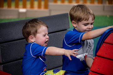 Younger brother throwing tantrum while older brother plays on playground equipment