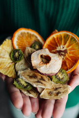 A woman in a green sweater holds dried fruit frips in her hands. Dried oranges, apples, kiwi, bananas, pears, pineapples. Healthy snack or breakfast