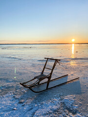 VIntage wooden kicksled on lake in sunset