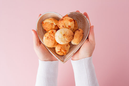 Cheese bread (brazilian Pao de Queijo mineiro) and coffee, heart-shaped plate, woman's hand, top view flat lay