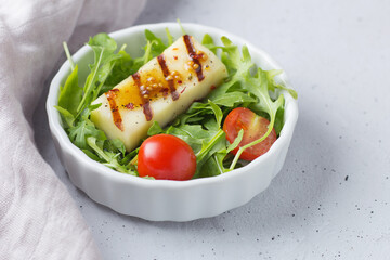 Portion of salad with fried halloumi cheese, cherry tomatoes,arugula in a plate on a gray background with textiles. healthy food. copy space.