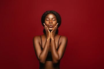 Sending a kiss with a blowing kiss. Fashion portrait of young african american female model posing against red background - Powered by Adobe