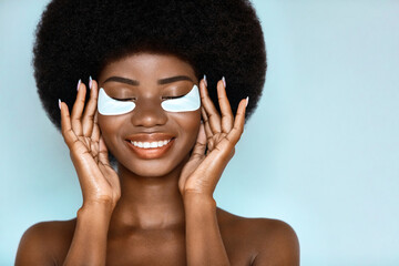 Beauty procedure. African american model posing with collagen patches on her eyes against blue...
