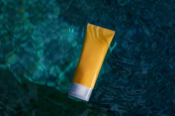 Skin hydration. Yellow tube of cream with a mockup in the blue transparent water. Skin care and hydration concept.