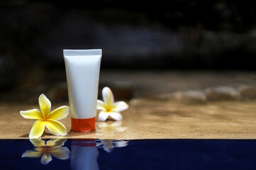 Beauty product. The white tube with a cosmetics product with a mockup and copy space is reflected in the water with plumeria flower. Skin care cream.