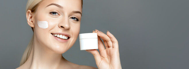 Skincare. Skin treatment. Beuauty portrait of a young woman holding and applying cream on her face