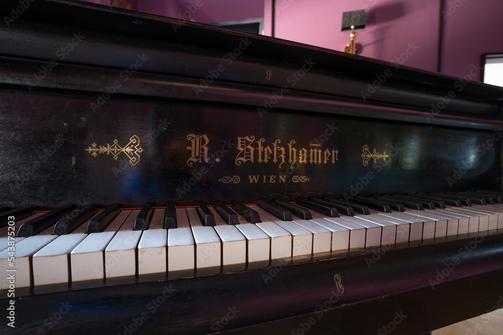 Aufkleber a piano with a black case and a white keyboard with writing on it and a mirror behind it in a room.