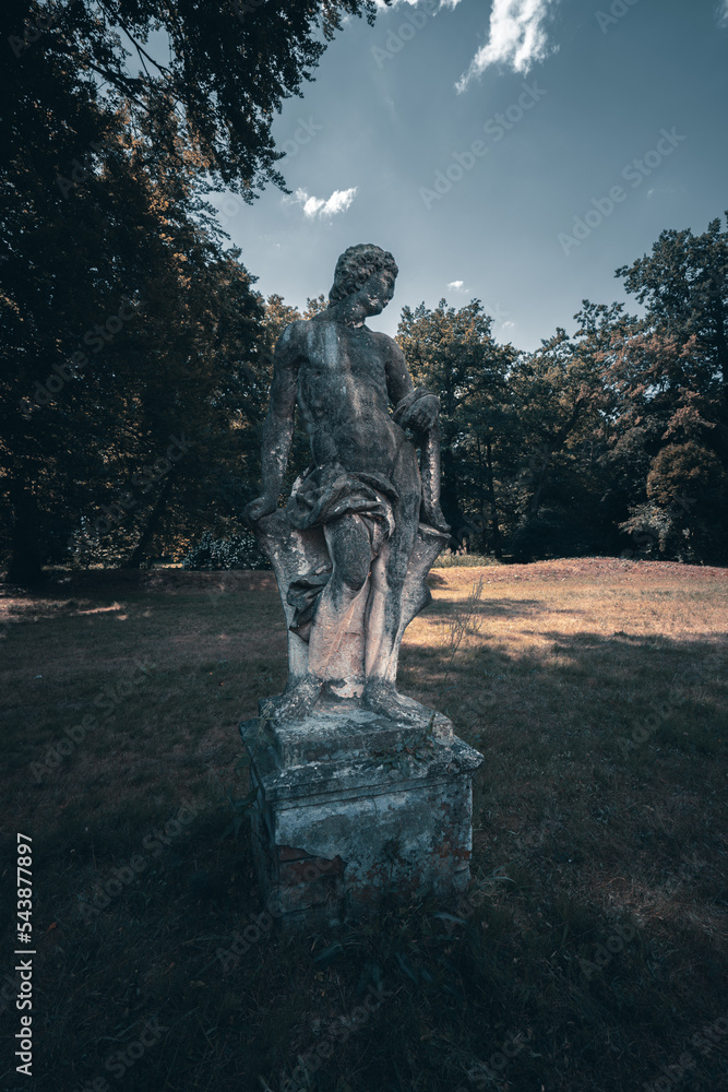 Poster a statue of a man sitting on a stone block in a park with trees in the background and a blue sky wit