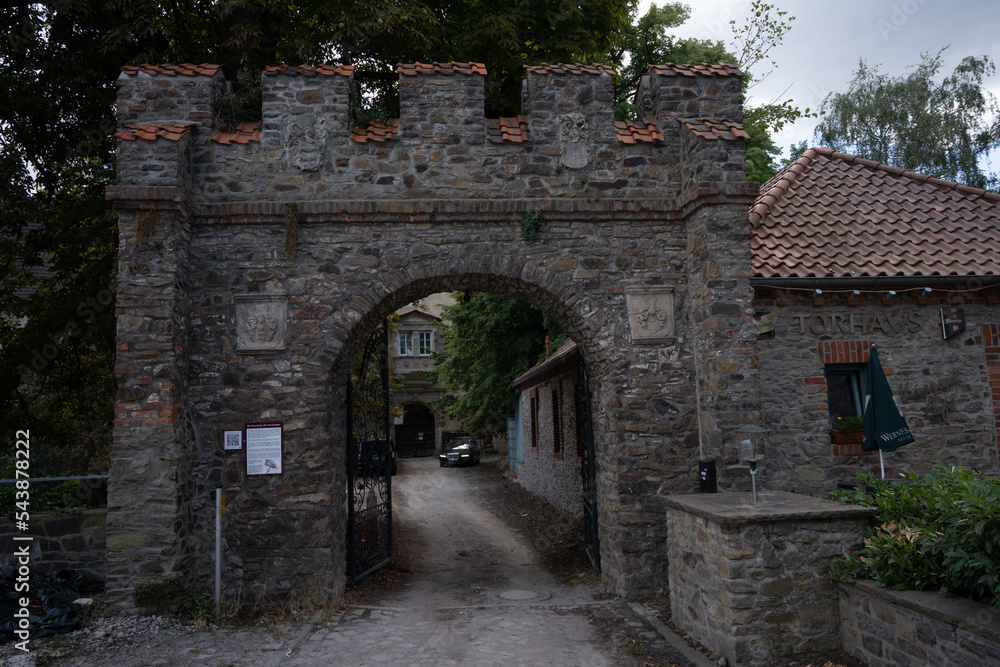 Poster a stone gate with a brick building in the background and a car parked in the driveway behind it on a