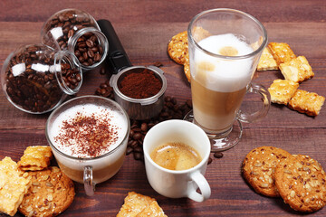 Breakfast with espresso, latte and cappuccino, sweets, holder with ground coffee, tamper and coffee beans on wooden table.