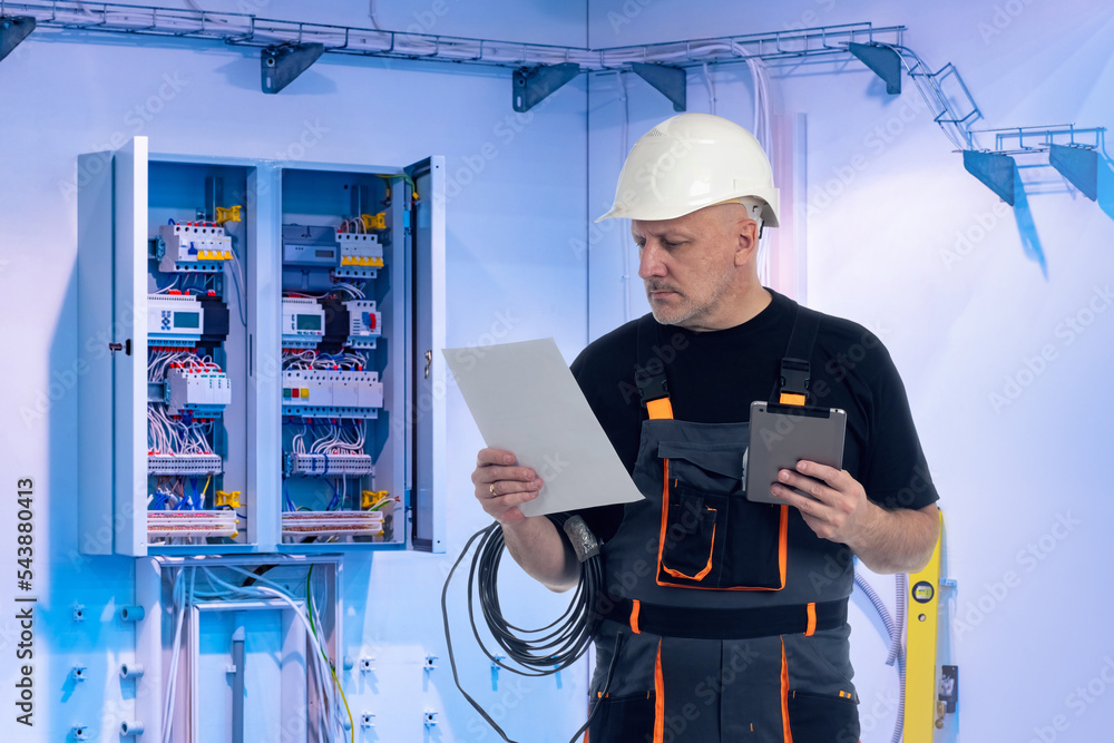 Poster man next to electrical panel. electrician at work. guy with tablet fixes electrical equipment. man e