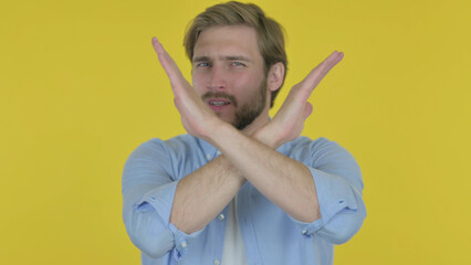 Rejecting Young Man with Arm Gesture on Yellow Background