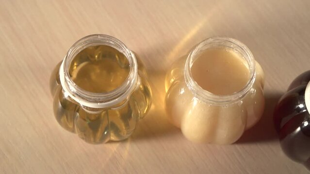Close up panning to three plastic jars of different kinds honey without caps on table. Light honey is Linden, dark honey is taiga, transparent honey is acacia