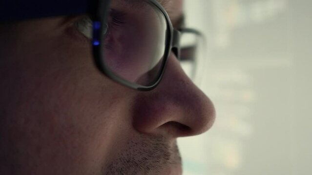 A programmer, a man in front of a computer, the code is reflected in the glasses. Working in IT, learning programming languages, developing applications and software.