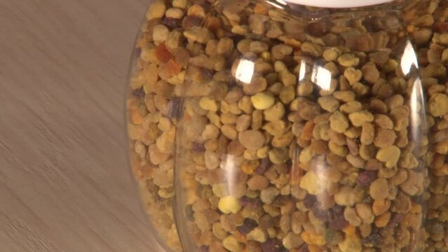 Close up of single plastic jar of pollen with white cap on table manually rolling artifically lighted