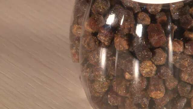 Close up panning of single plastic jar of perga with white cap on table artifically lighted