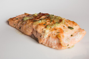 Close-up of a lemon salmon loin with garlic and parsley on an elegant white plate. Fish and healthy food