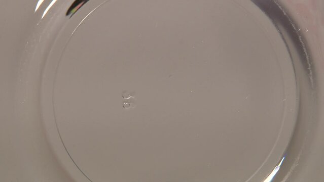 Close up of transparent glass plate with pouring honey shooted from below trough the plate. Artifical lighting indoor. Grey background