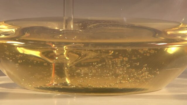 Close up of transparent glass plate on the table with pouring honey shooted from side trough the plate. Artifical lighting indoor