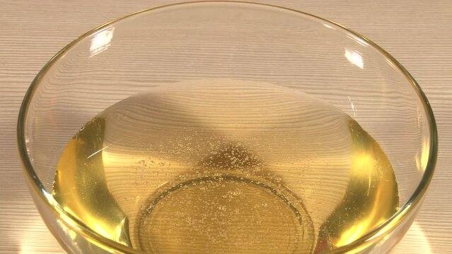 Close up of transparent glass plate standing on table with pouring golden honey shooted from above. Artifical lighting indoor