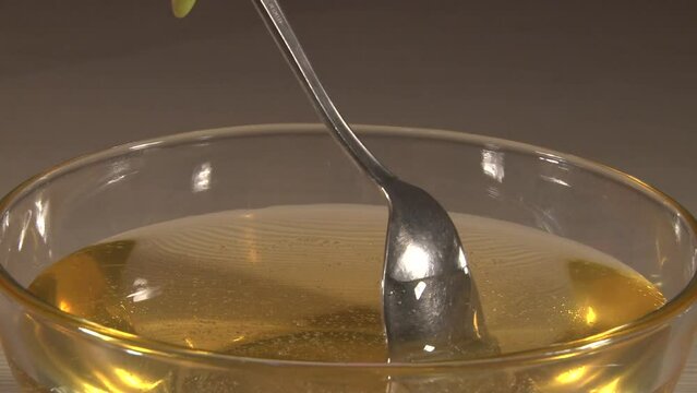 Close up of transparent glass plate full of honey stiring with a spoon shooted from side but metal spoon
