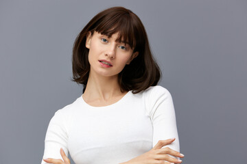 Fototapeta premium a sweet, beautiful, happy woman smiles pleasantly looking at the camera standing on a gray background in a white T-shirt