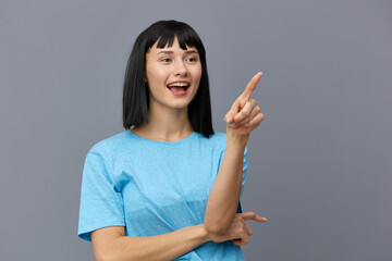 an admiring woman stands on a gray background in a blue T-shirt smiling slightly holding one hand...