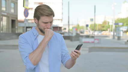 Upset Man Reacting to Loss on Smartphone Outdoor