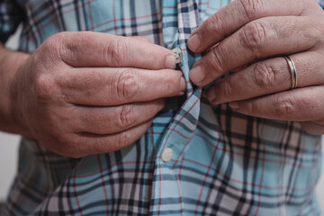 Close-up of a man's hands buttoning a plaid shirt.