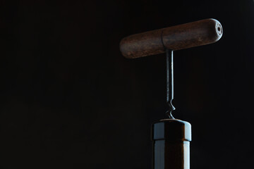 Corkscrew and cork. A wooden corkscrew is stuck in the cork. The neck of the bottle. Dark background. - obrazy, fototapety, plakaty