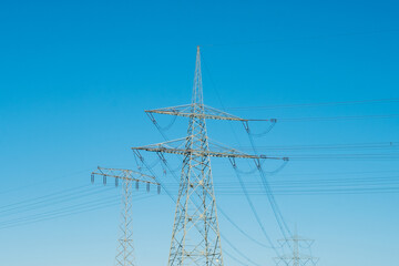 Energiekosten, Strommast auf Feld vor blauem Himmel - 543894249
