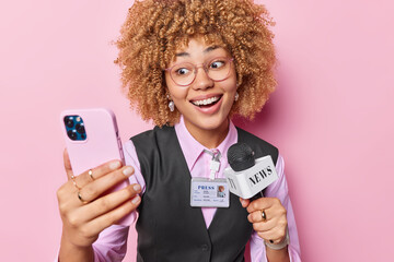 Positive curly haired woman in formal clothes takes selfie via smartphone or records livestream...
