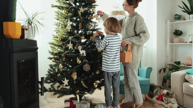Child and mother, family decorating Christmas tree in pajamas in cozy home interior