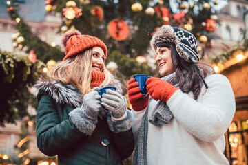 Best friends enjoying mulled wine on Christmas market looking at camera - 543897853