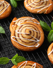 Freshly baked sweet cinnamon swirls with icing on cooling rack. Sweet food