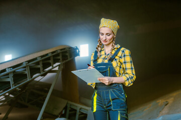 Fototapeta na wymiar Farmer woman in the granary keeping track of the harvest by taking notes on clipboard